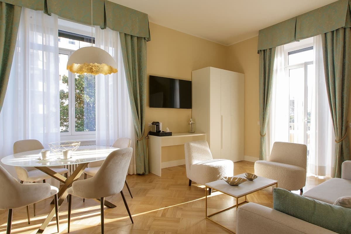 A modern living room with a round dining table, two armchairs, a sofa, and a TV mounted on the wall.