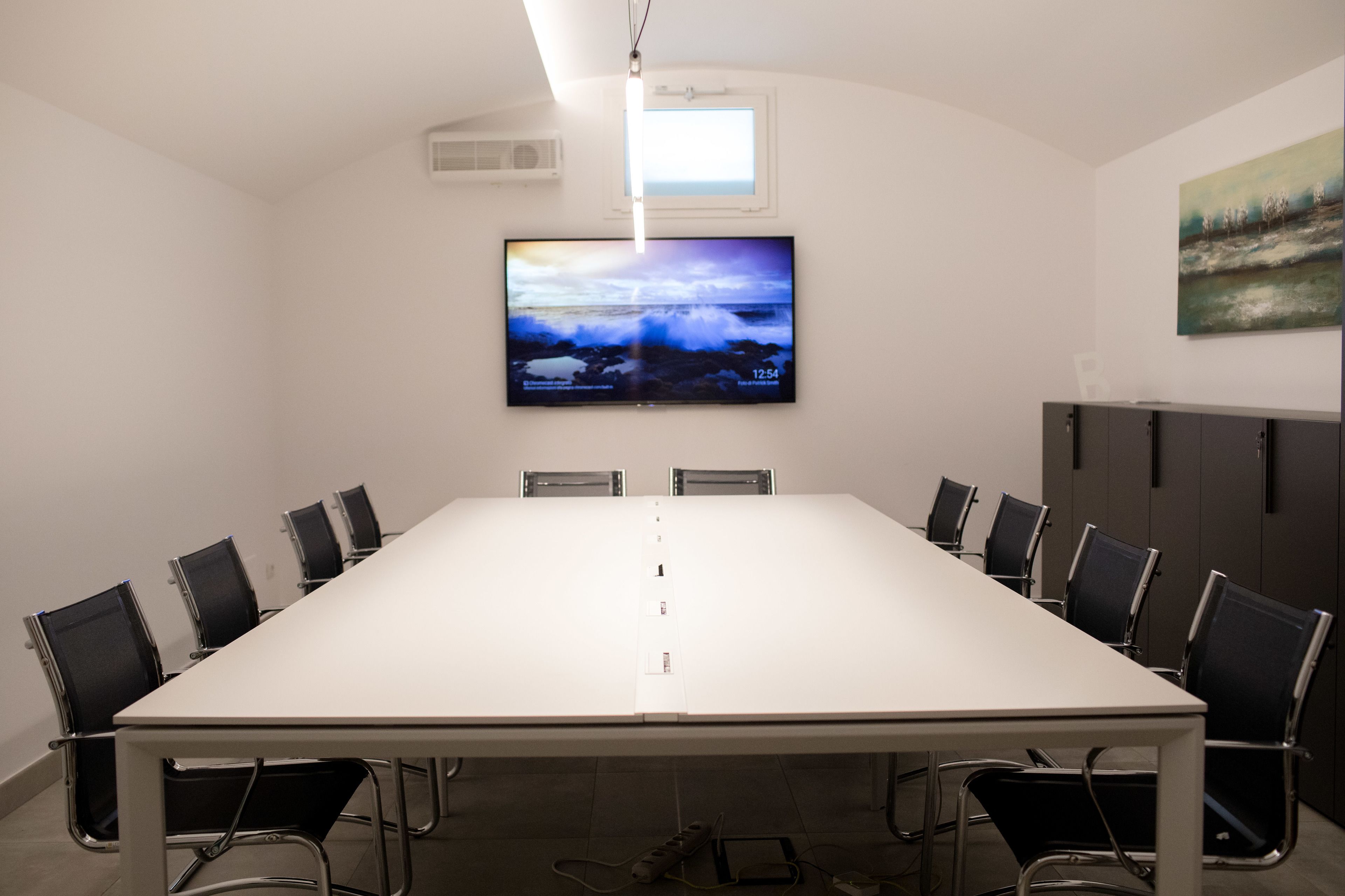 Ein Konferenzraum mit langem Tisch, schwarzen Stühlen, einem Wand-Fernseher und einem Gemälde an der Wand.