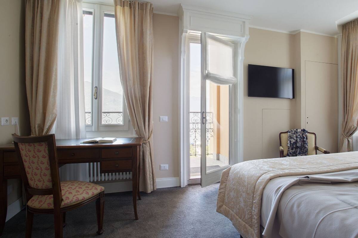 A hotel room with a bed, a desk, a chair, a TV, and a balcony door.
