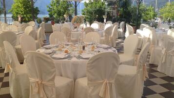 Une salle de banquet avec des tables rondes dressées pour un événement formel, entourées de chaises recouvertes de blanc et ornées de nœuds.