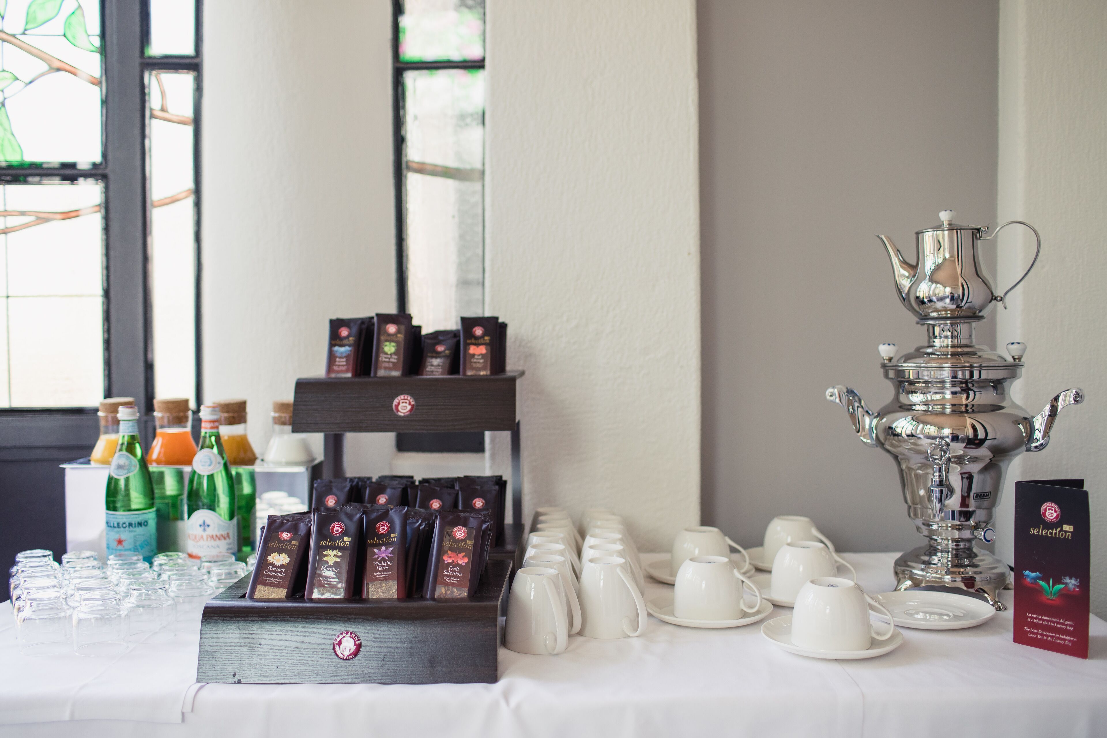 Ein Frühstücksbuffet mit Kaffee- und Teesorten, einer silbernen Teekanne sowie verschiedenen Tassen und Untertassen auf einem Tisch.