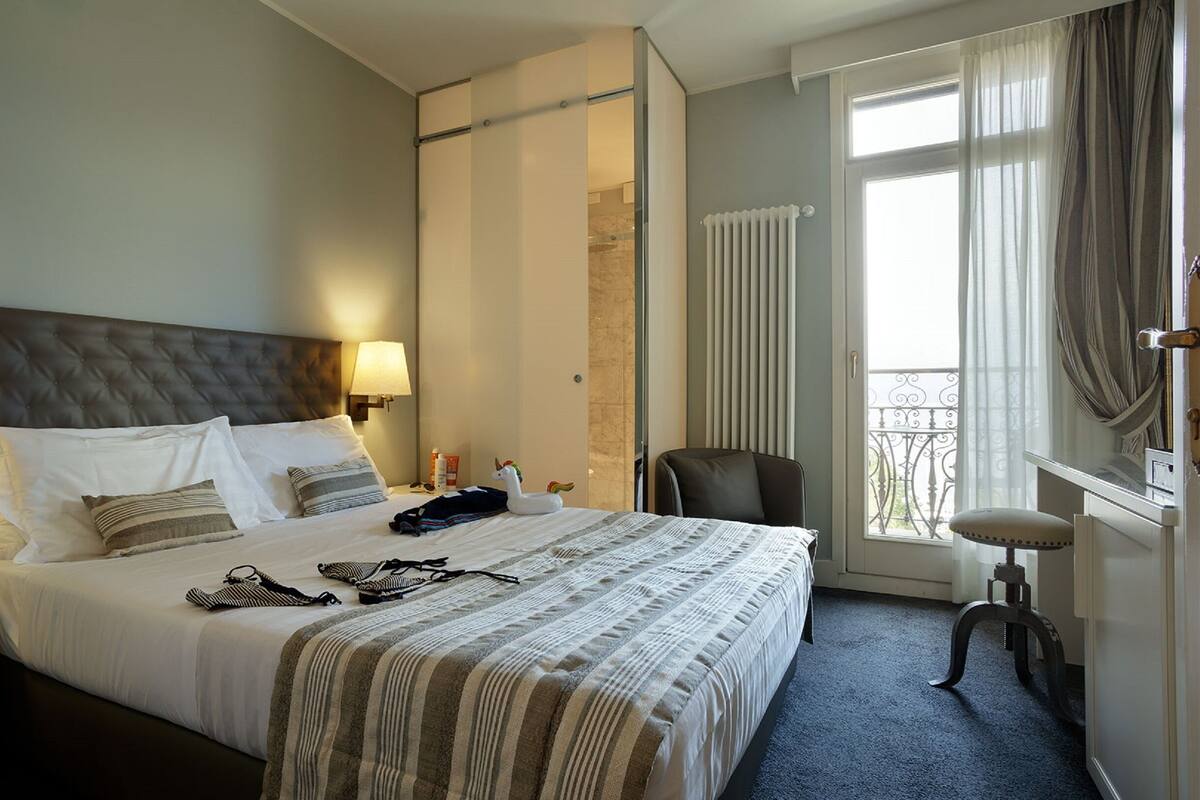 A hotel room with a large bed, two bedside lamps, a chair, a small table, and a window with curtains.