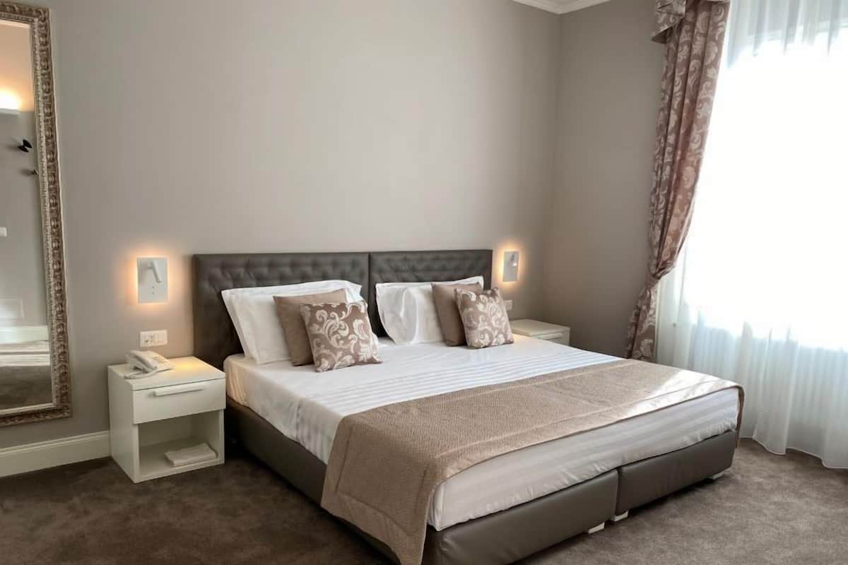 A neatly made bed with a headboard, a bedside table with a lamp, and a large mirror on the wall.