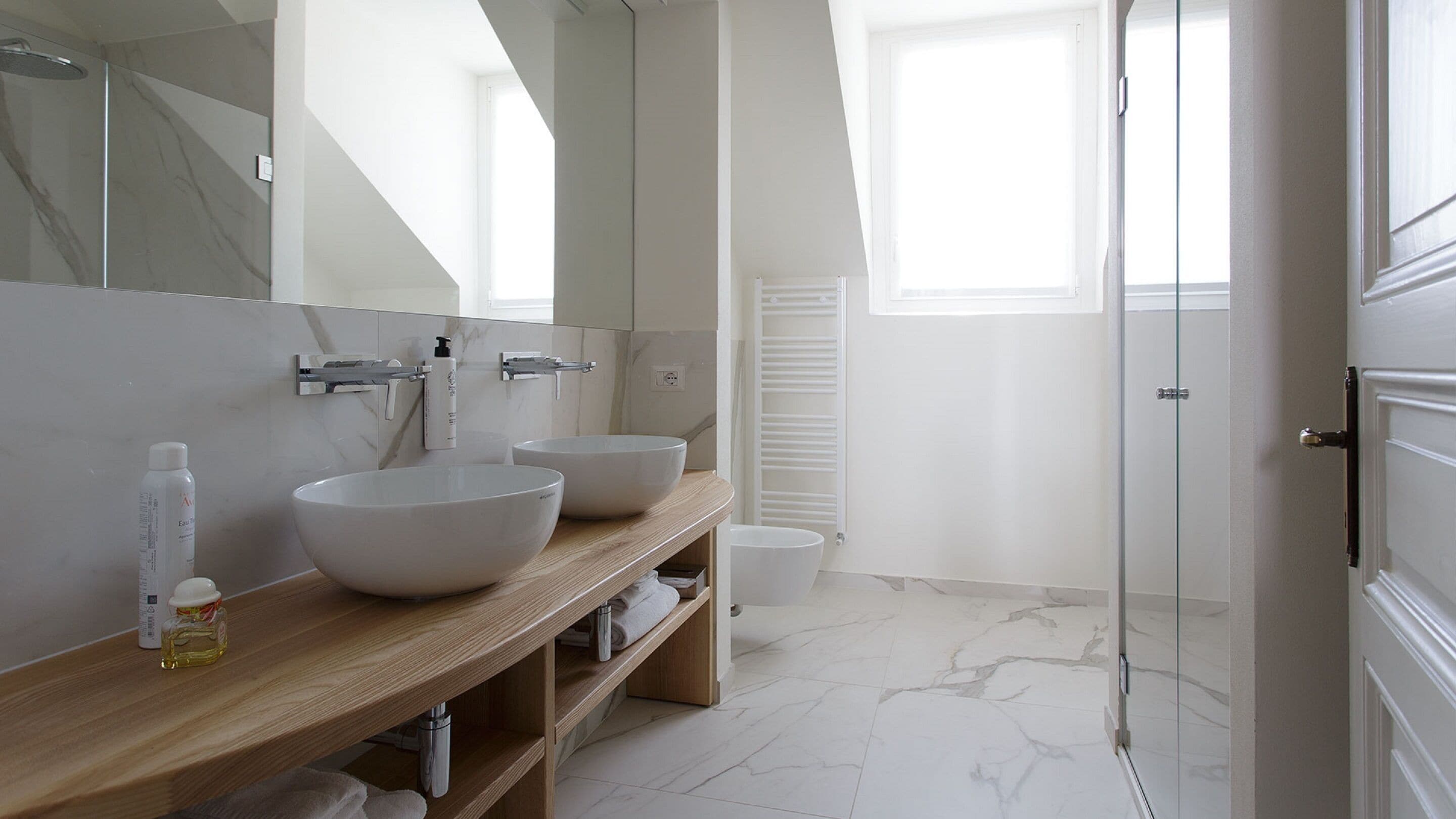 Ein modernes Badezimmer mit zwei großen weißen Waschbecken, einem Holz-Waschtisch, einem Spiegel und einer Glasdusche.