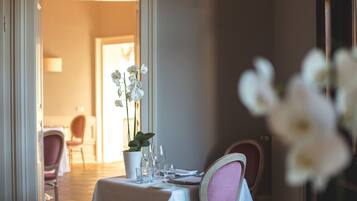A dining table set with white tablecloth, pink chairs, and a potted orchid.