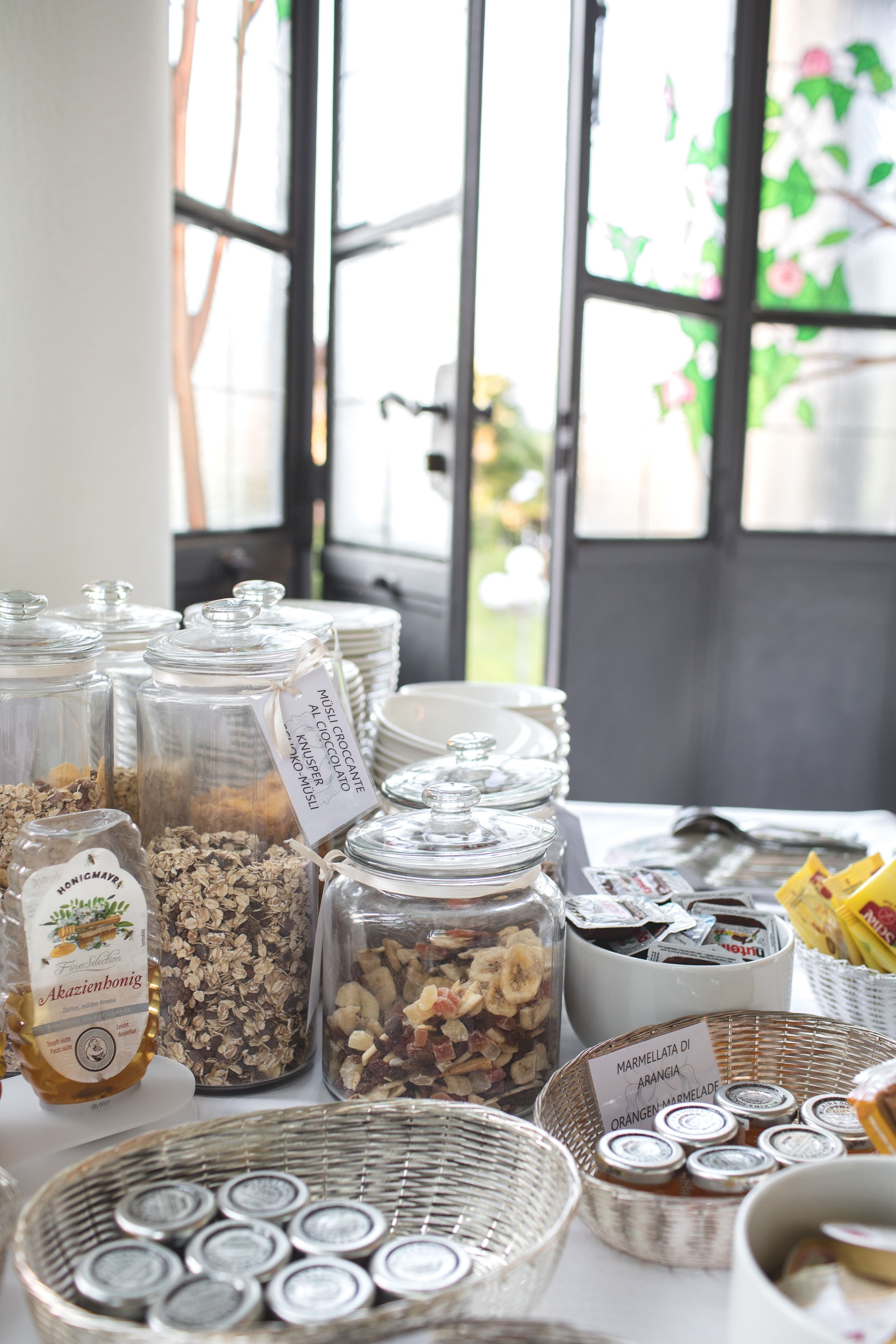 Une table sur laquelle se trouvent divers aliments et récipients, notamment des pots de granola et de confiture de marmelade, ainsi qu’une bouteille de miel.