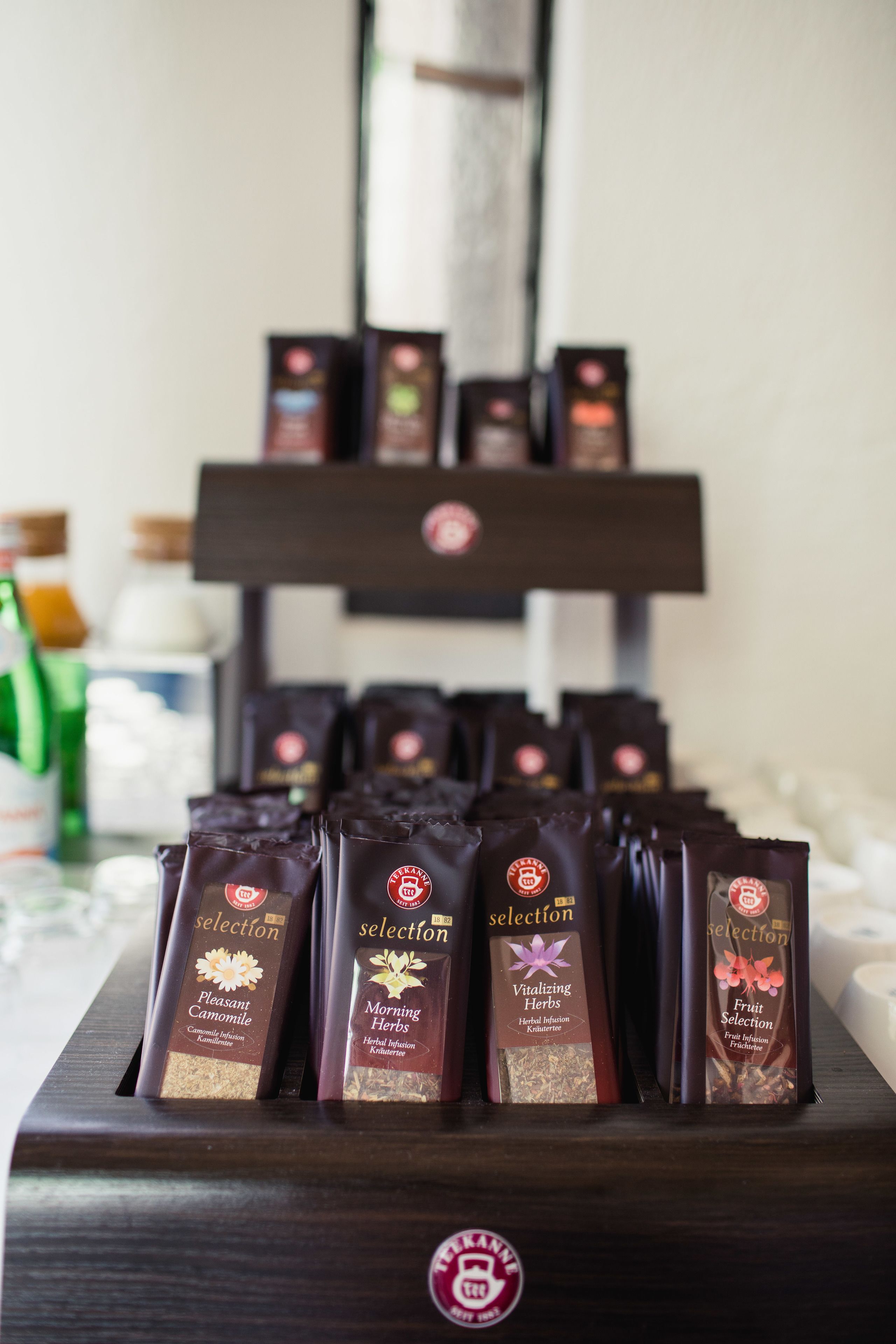 Eine Präsentation von Kräutertee-Produkten in dunkler Verpackung, mit Etiketten, die verschiedene Geschmacksrichtungen wie ‚Pleasant Camomile’ und ‚Vitalizing Herbs’ ausweisen.