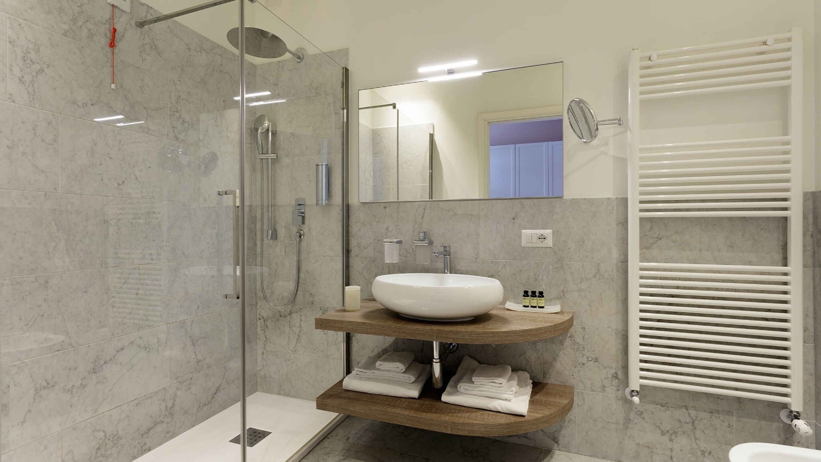 Un baño moderno con ducha envuelta en vidrio, un lavabo blanco y un mueble de tocador de madera.