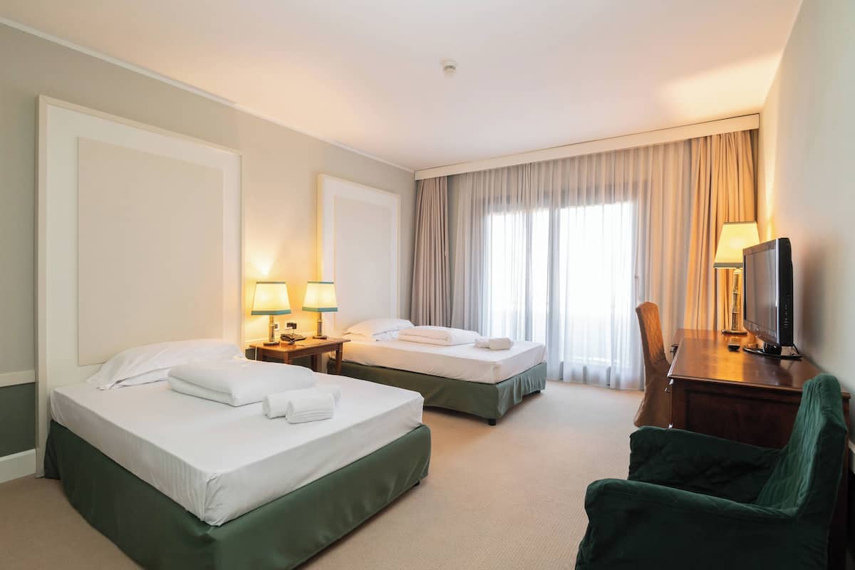A hotel room with two beds, a desk with a television, and a chair.