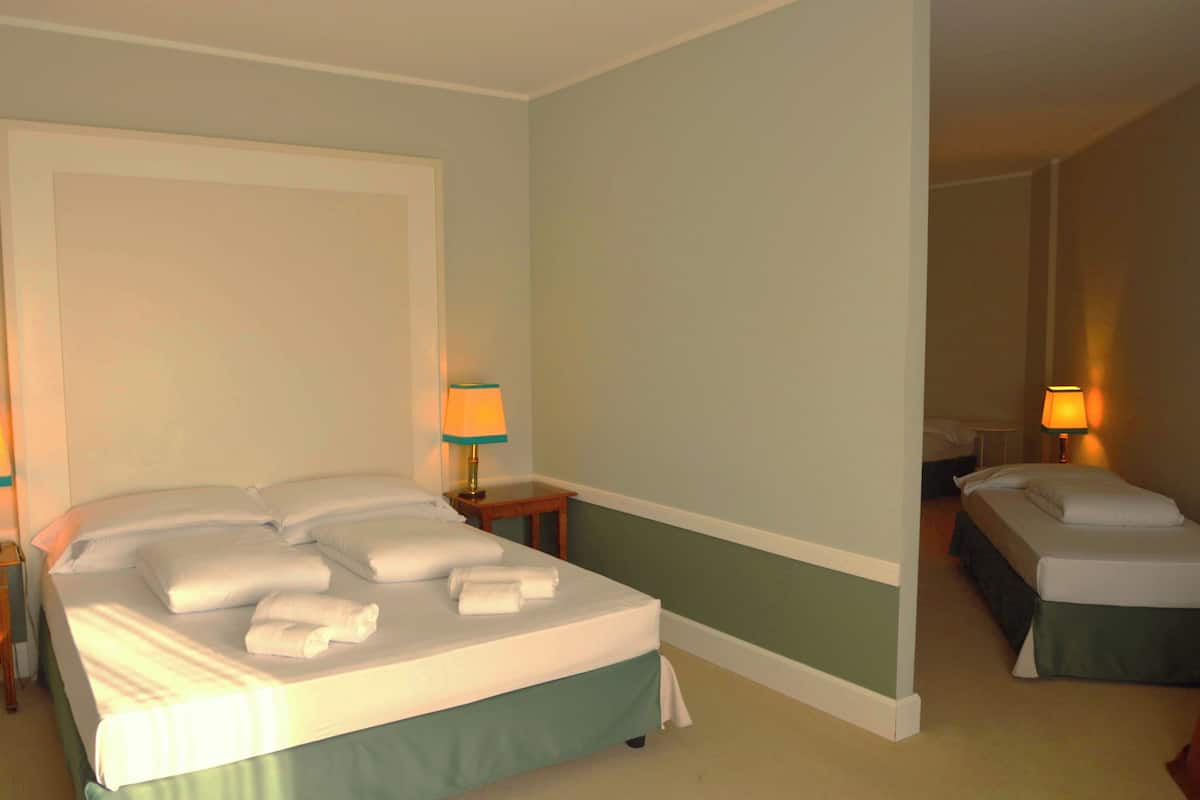A hotel room with a large bed, a smaller bed, two bedside tables with lamps, and a nightstand.