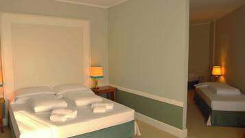 A hotel room with a large bed, a smaller bed, two bedside tables with lamps, and a nightstand.