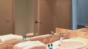 A bathroom with a marble vanity, a large mirror, and a white sink. There are towels stacked on the vanity and a shower visible in the background.
