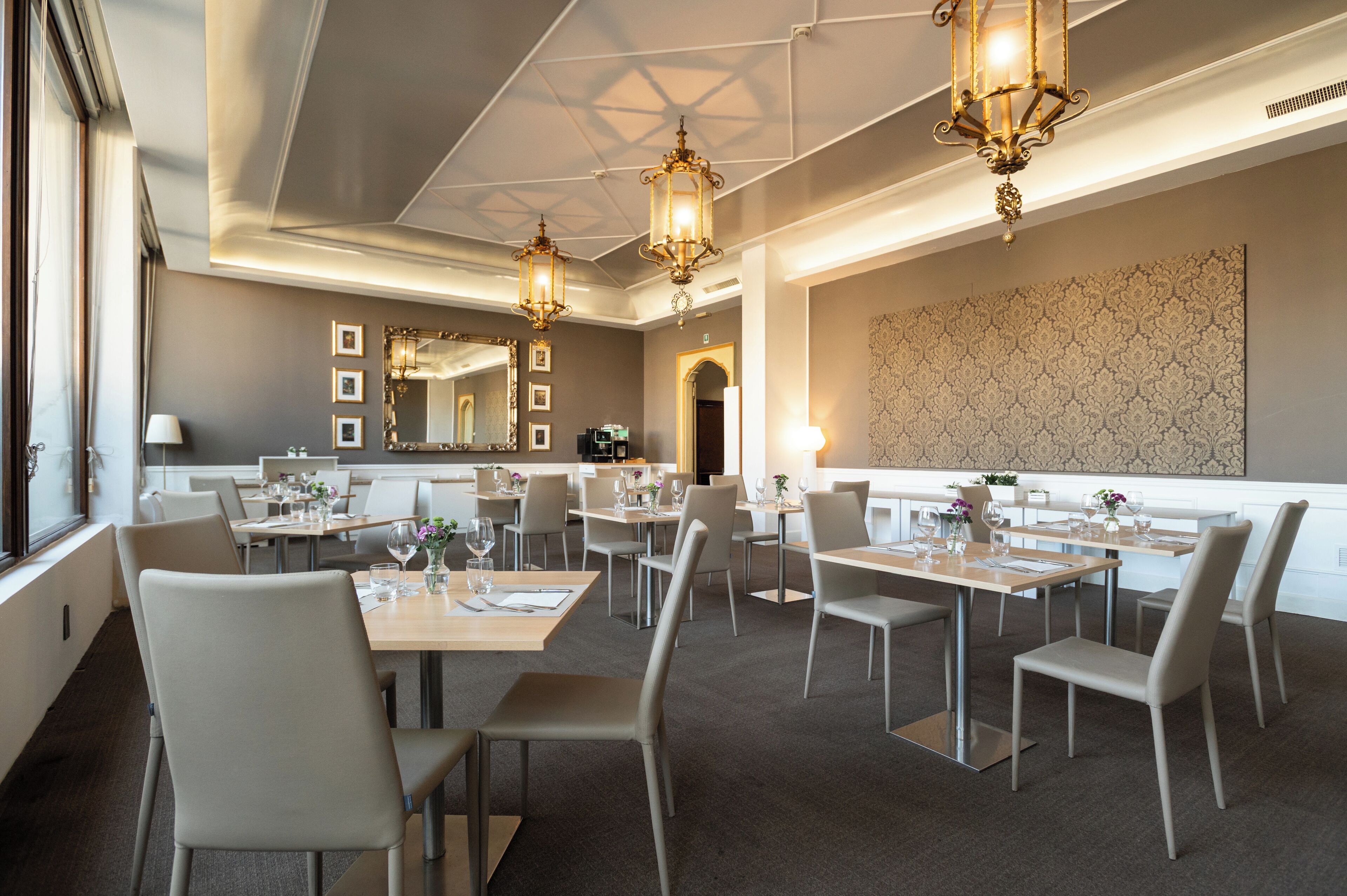 A modern dining area with tables and chairs, chandeliers, and a large mirror.