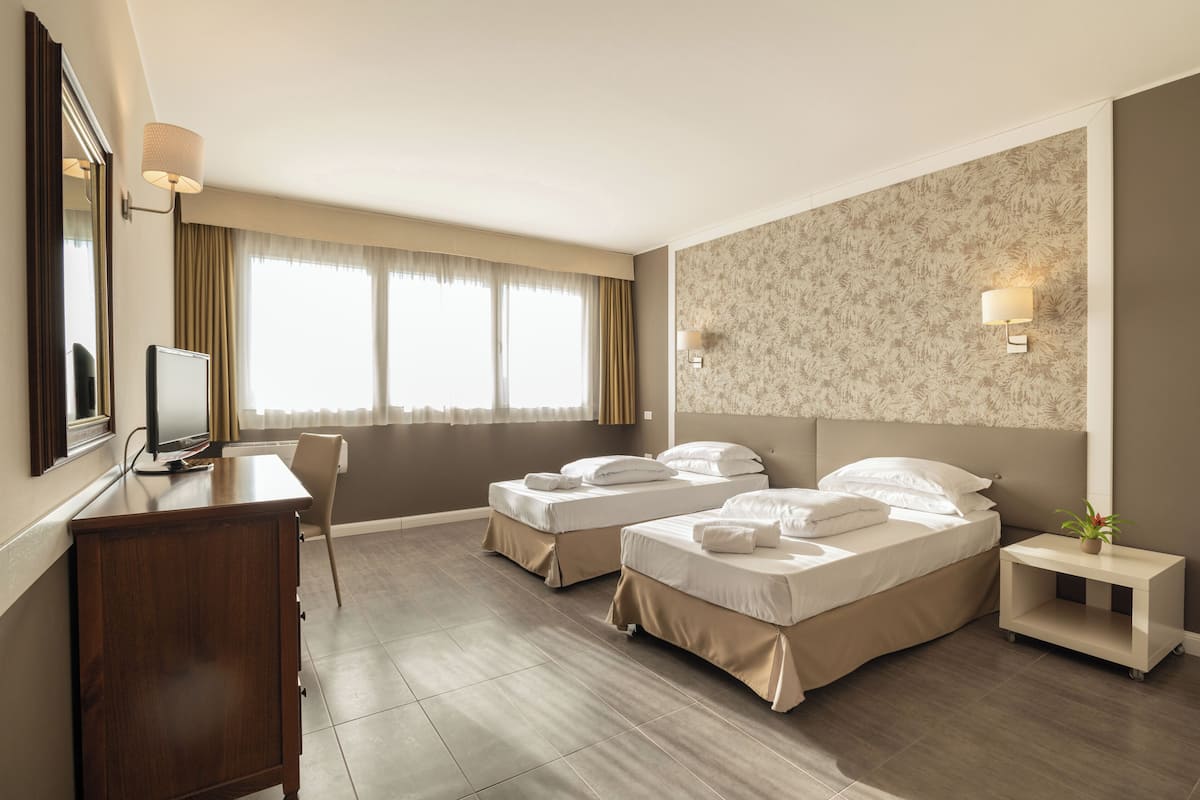 A hotel room with two beds, a desk, a television, and a small plant.