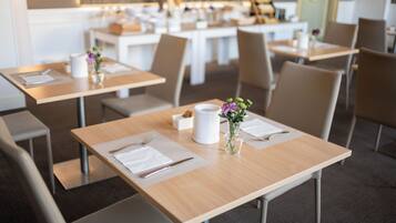 A modern dining area with neatly arranged tables, each set with cutlery, napkins, and a small vase with flowers.