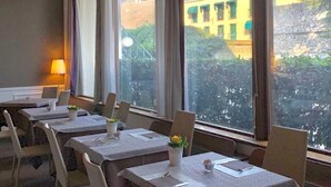 A dining area with tables set for four, large windows with a view of buildings and greenery. - Blue Dream Hotel (Monselice)