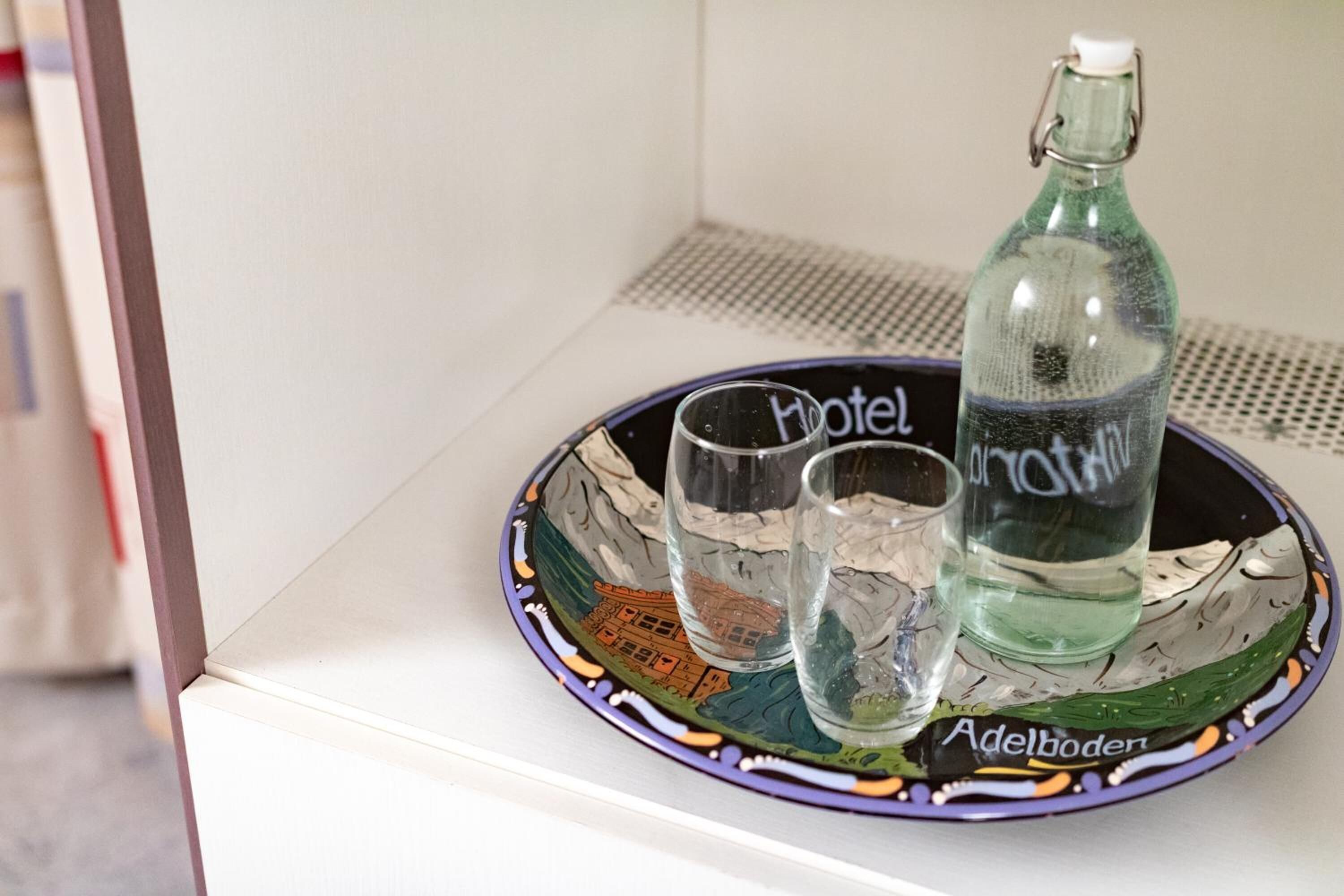Una botella de vidrio y dos vasos sobre una bandeja con el nombre y la ubicación de un hotel.