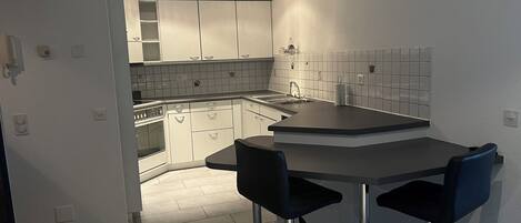 Una cocina moderna con armarios blancos, una encimera negra y dos taburetes de bar.