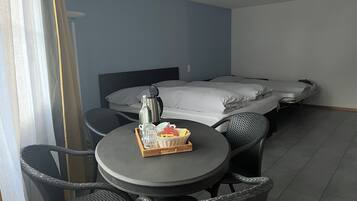 Een hotelkamer met een bed, een ronde tafel met stoelen, een koffiezetapparaat en een mand met brood op de tafel.