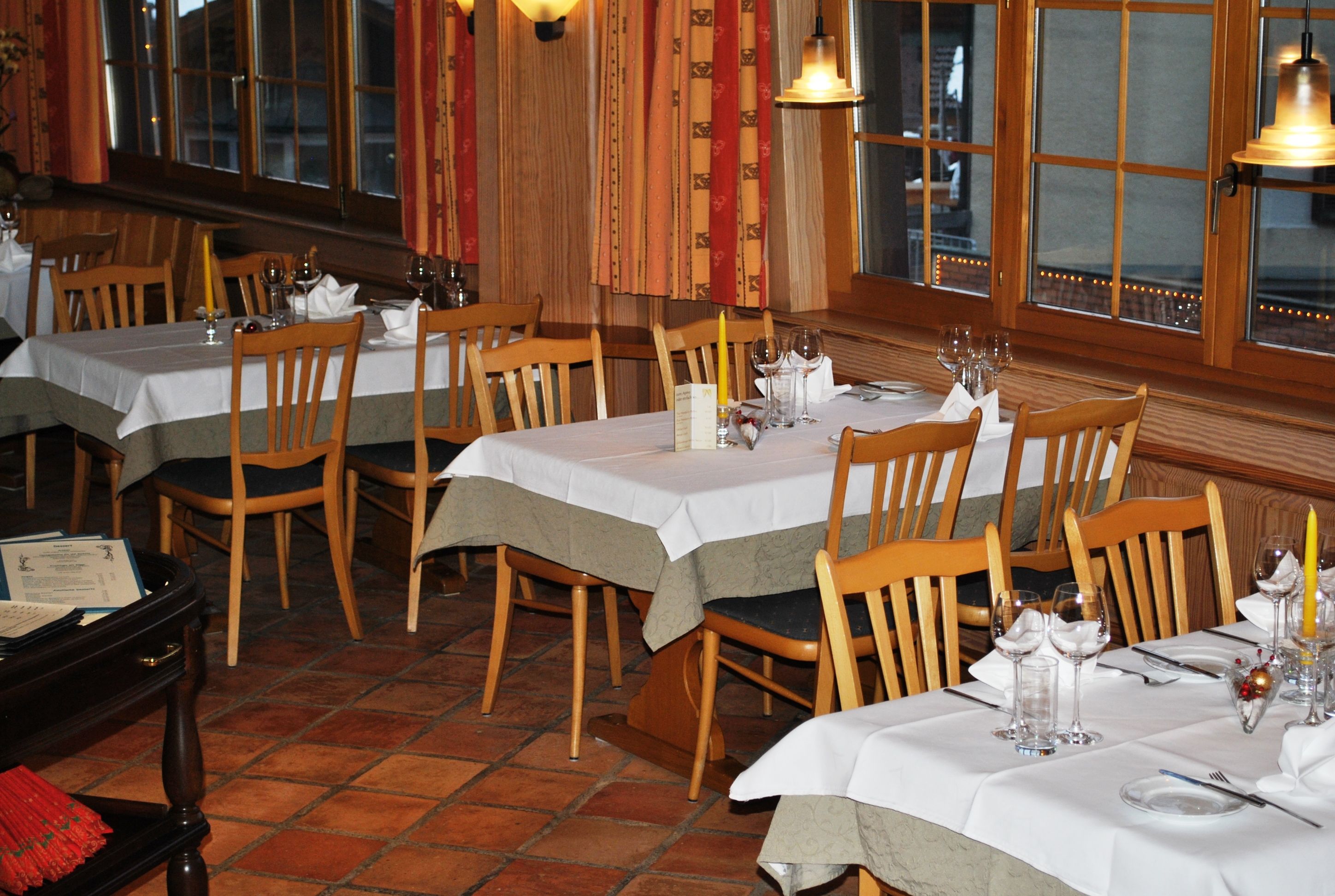A restaurant with multiple tables set for dining, wooden chairs, and a tiled floor.