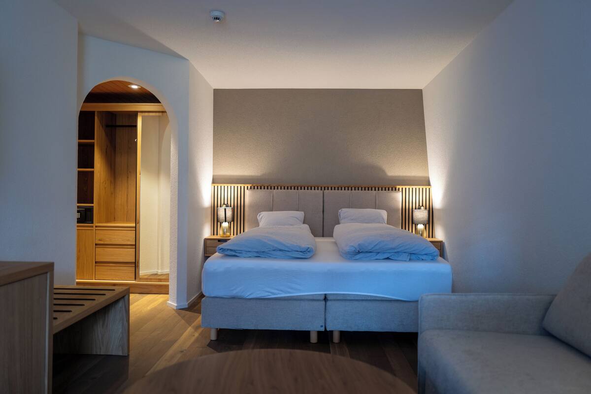 A modern bedroom with a double bed, bedside tables, a bench, and a wardrobe.