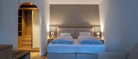 Un dormitorio moderno con una cama doble, mesitas de noche, un banco y un armario.