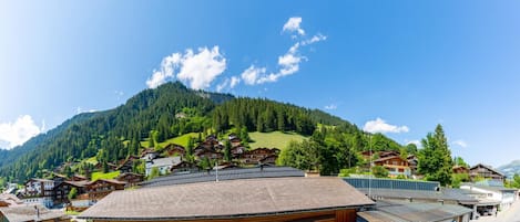 A mountain village with traditional wooden houses, a central building with a sloped roof, and a clear blue sky.
