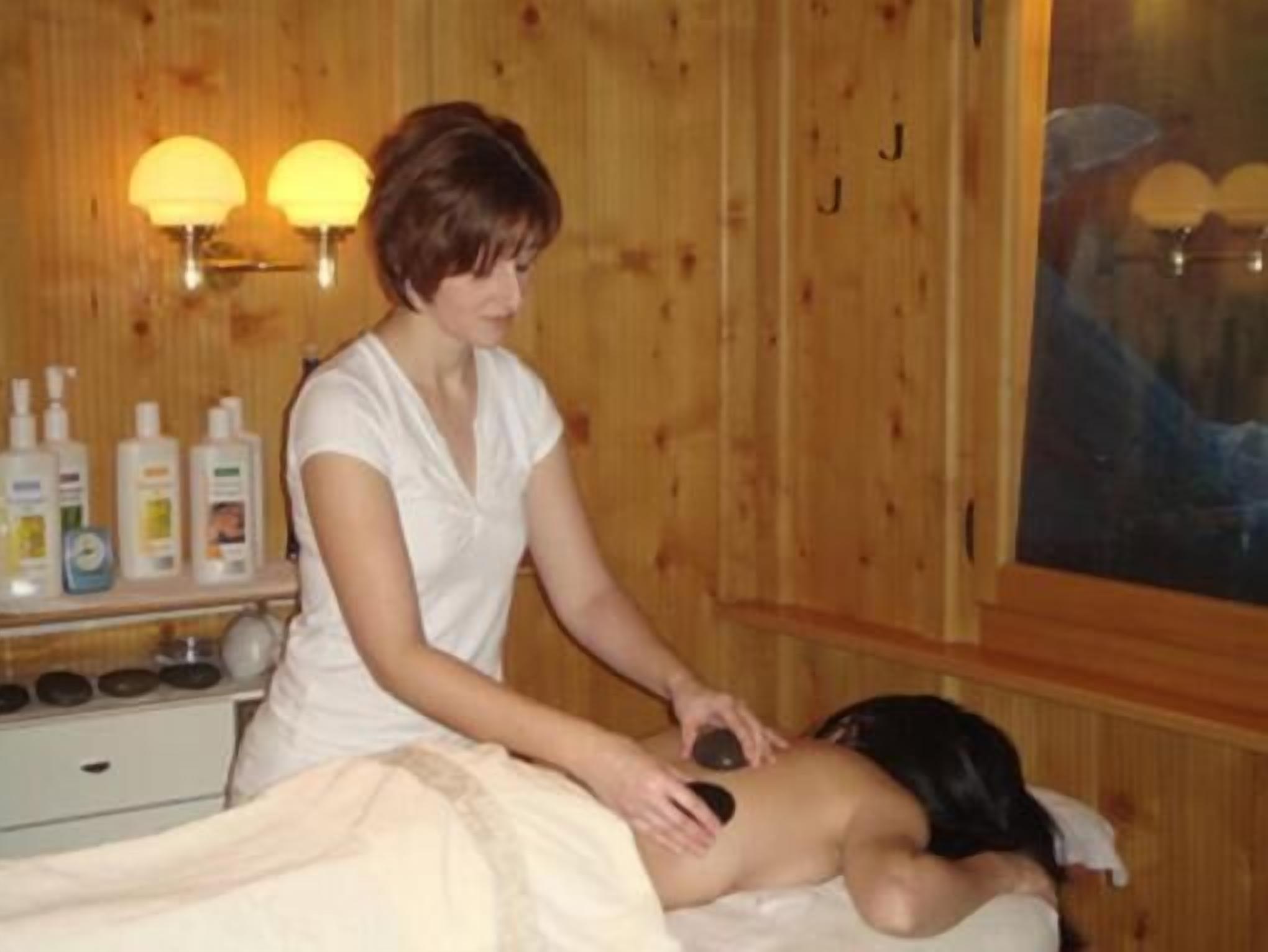 A massage therapy session in a room with wooden paneling, a massage table, and a shelf with bottles.
