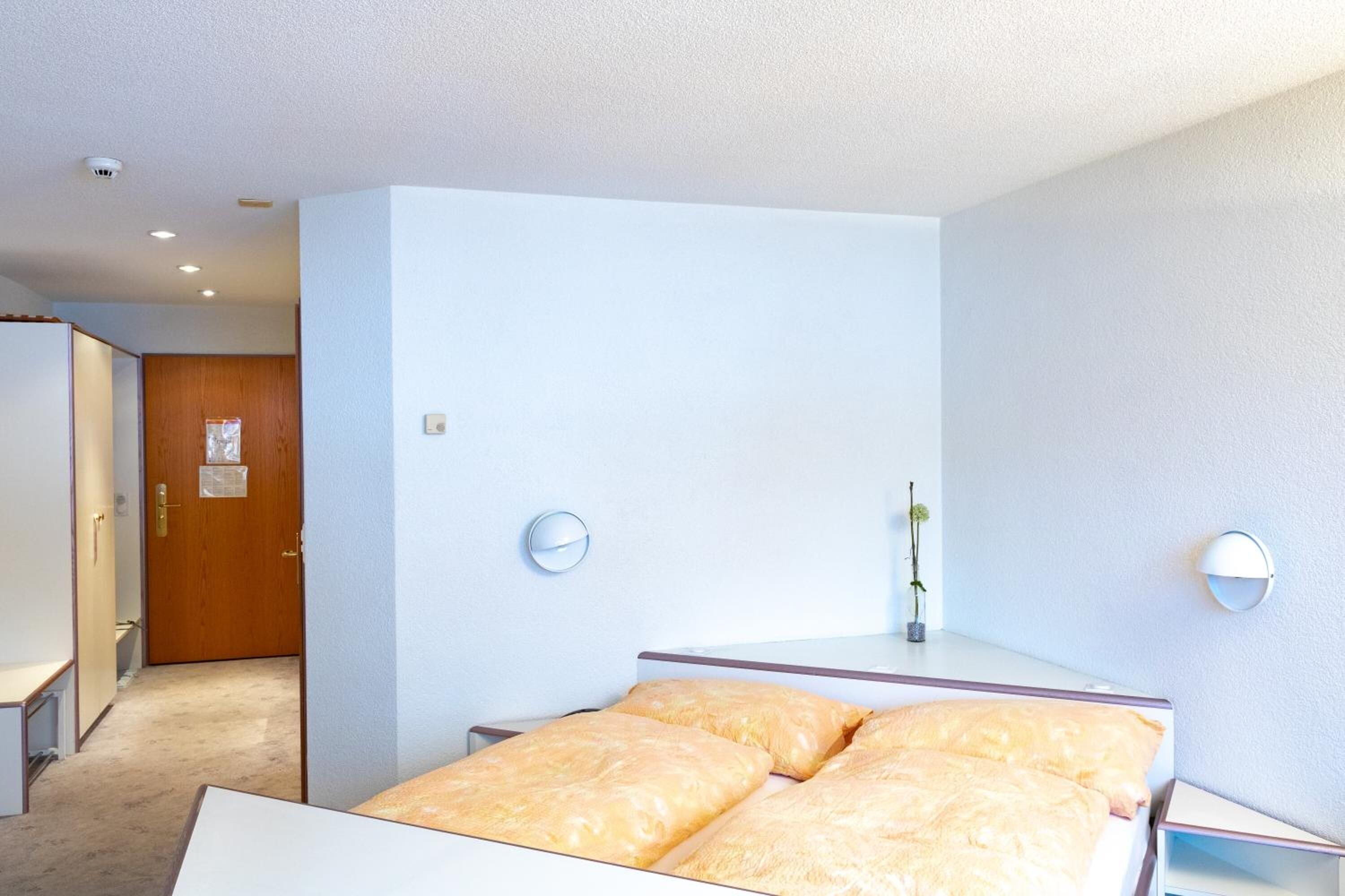 Habitación de hotel con cama, puerta de madera, una planta pequeña y un reloj de pared.