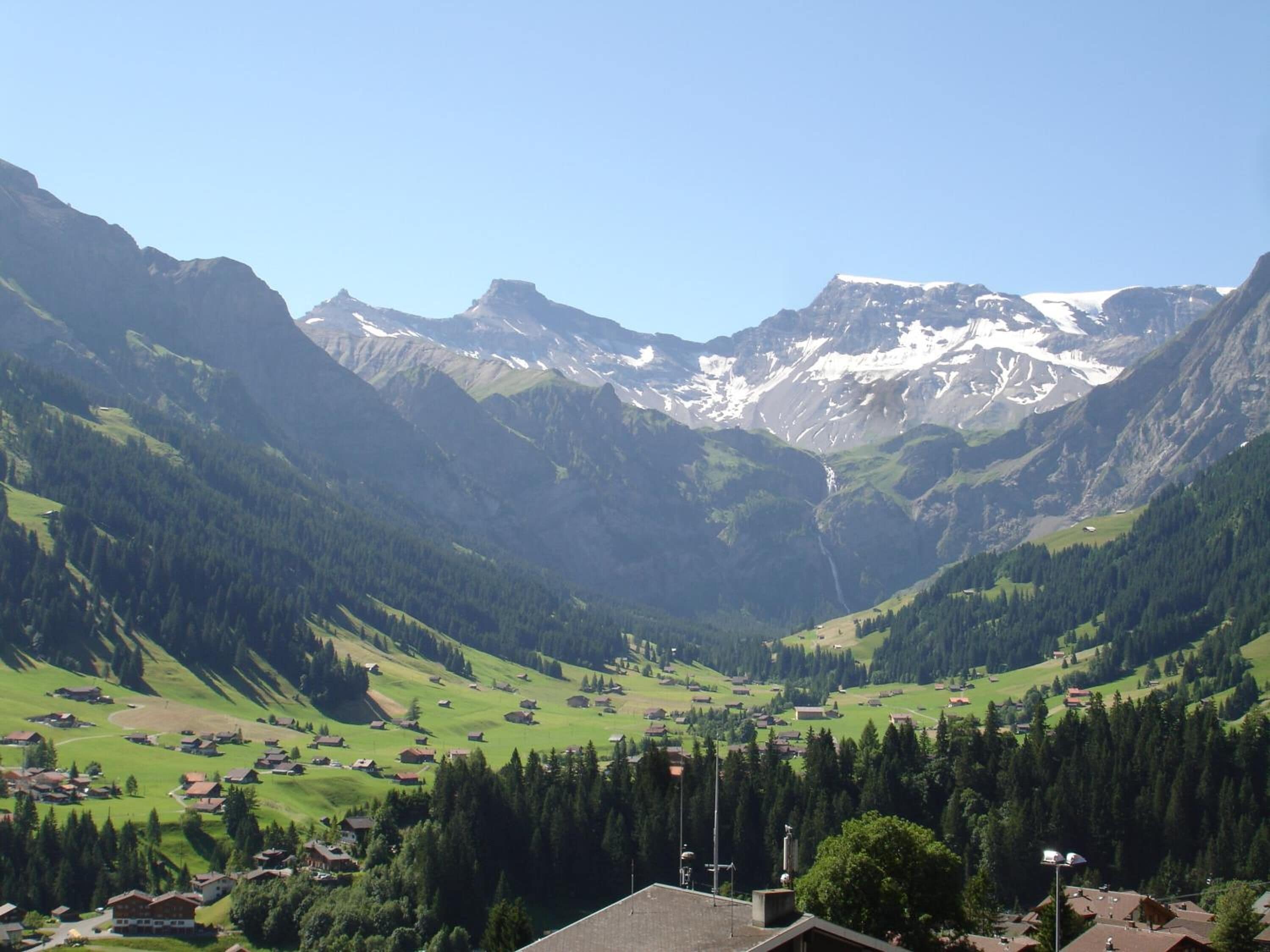 Eine gebirgige Landschaft mit einem Tal, Häusern und blauem Himmel.