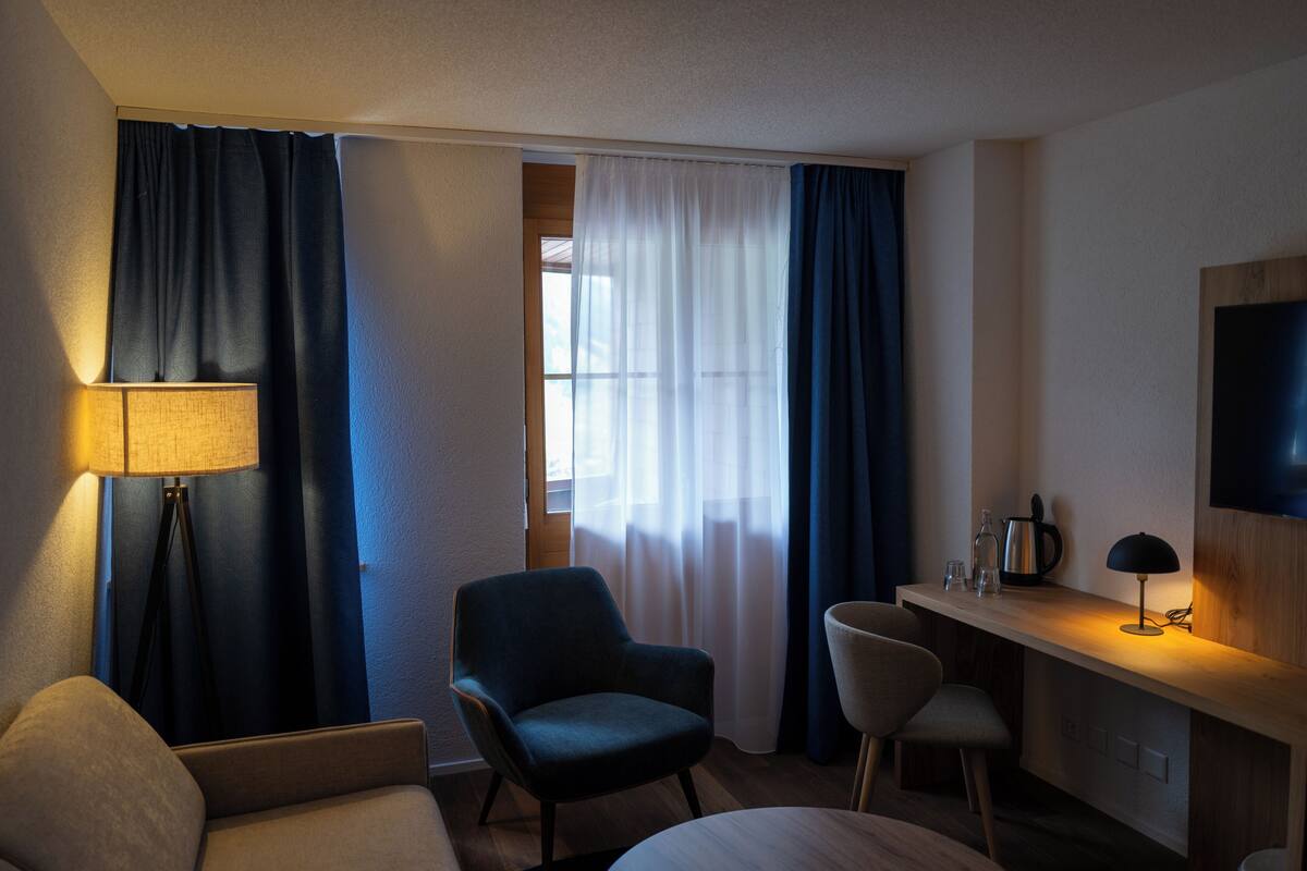 A hotel room with a bed, a desk, a chair, a lamp, and a TV.