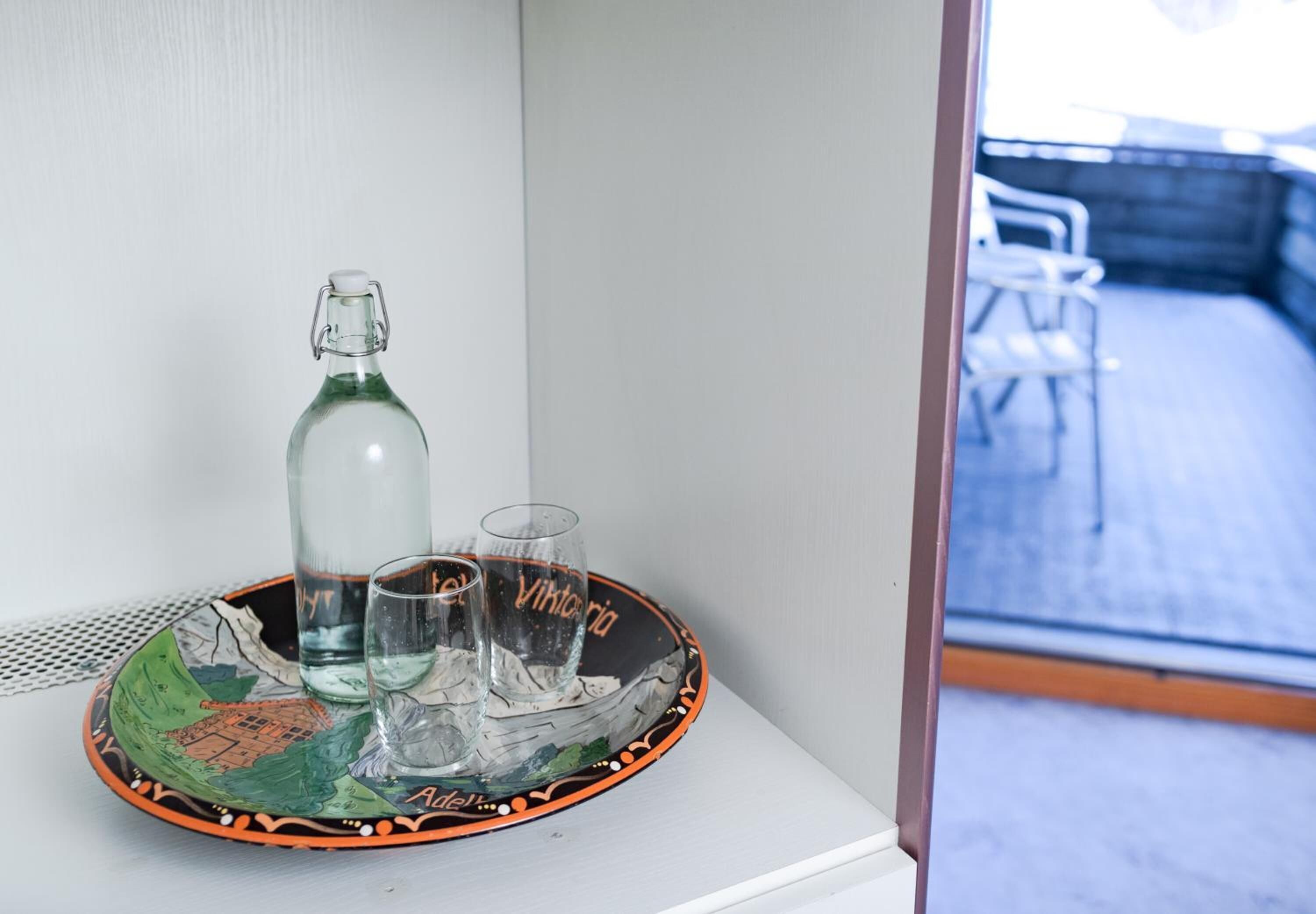 A glass bottle and two glasses on a decorative tray with a map design, placed on a white surface.