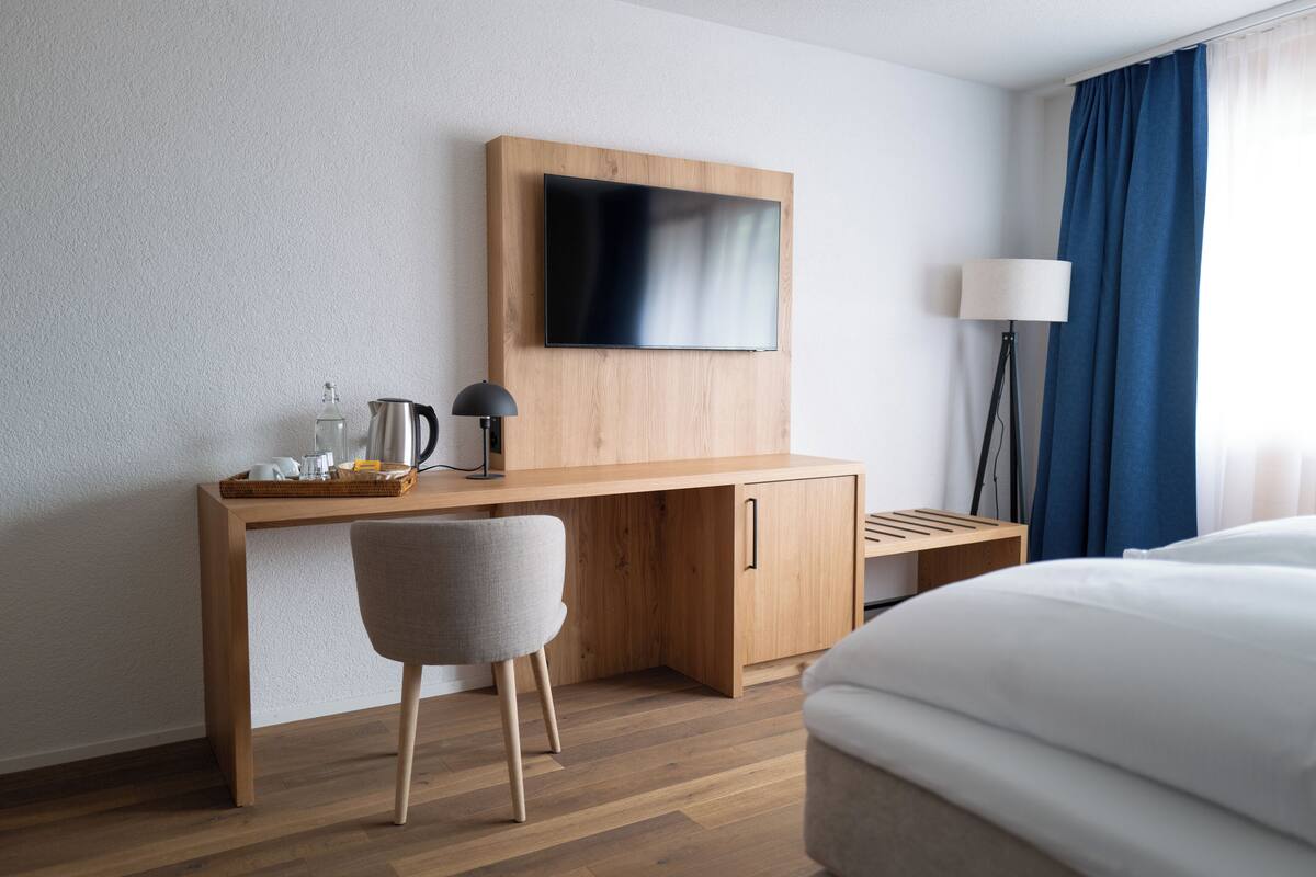 A hotel room with a wooden desk, a flat-screen TV, a lamp, and a bed.