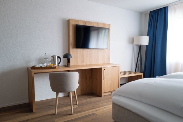 A hotel room with a wooden desk, a flat-screen TV, a lamp, and a bed. - Viktoria Eden (Adelboden)