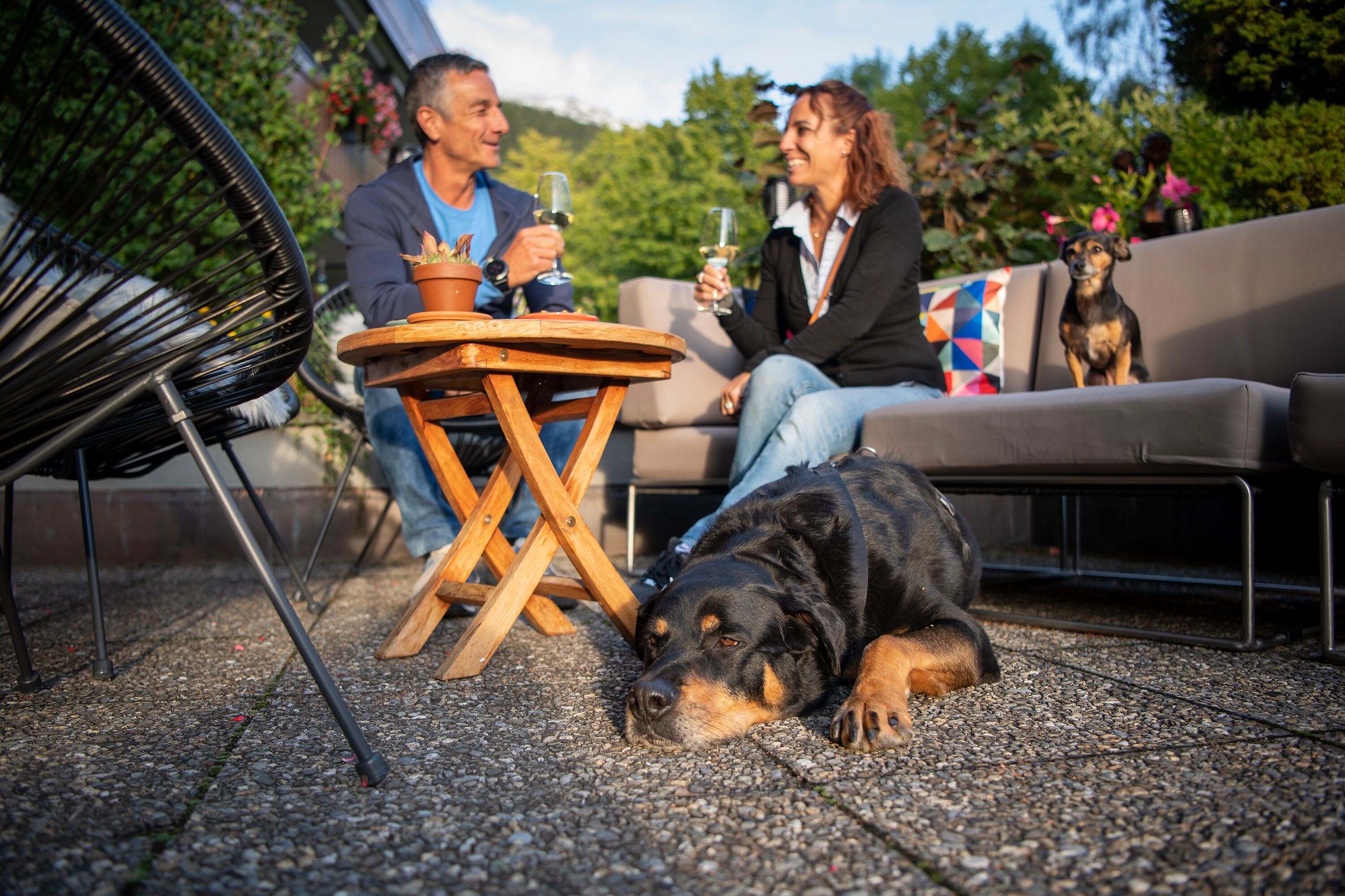 A patio with a round wooden table, a black metal chair, and a large dog lying on the ground.