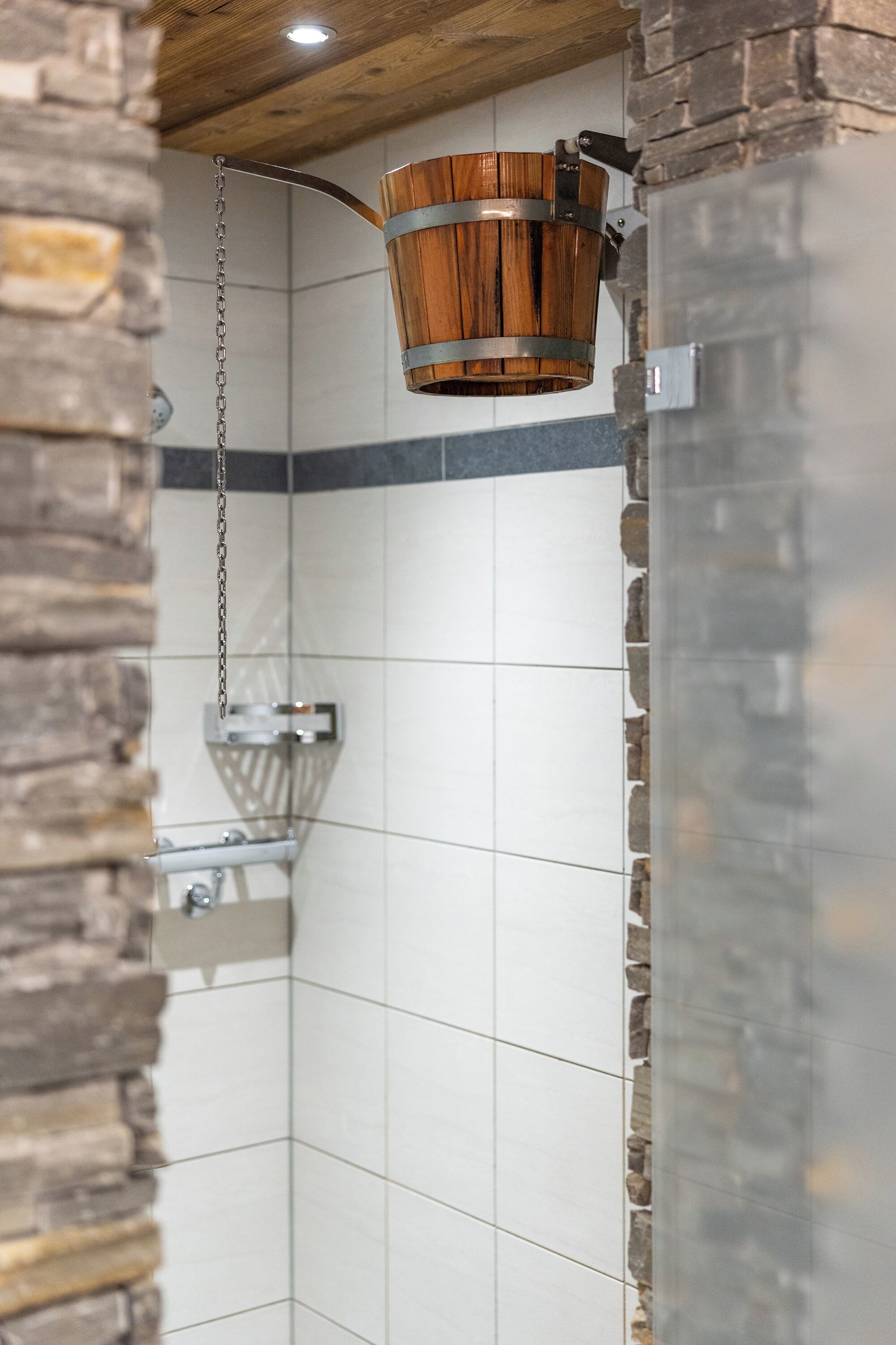 A shower area with a wooden bucket, stone wall, and tiled floor.