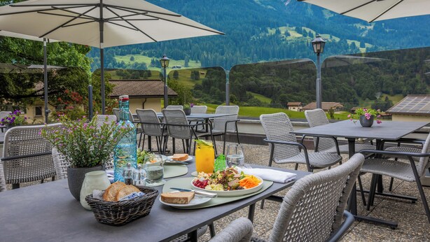 An outdoor dining area with tables, chairs, umbrellas, and a scenic mountain view. - Sunstar Hotel Klosters (Klosters-Serneus)
