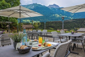 Un área de comedor al aire libre con mesas, sillas, sombrillas y una vista panorámica de la montaña.