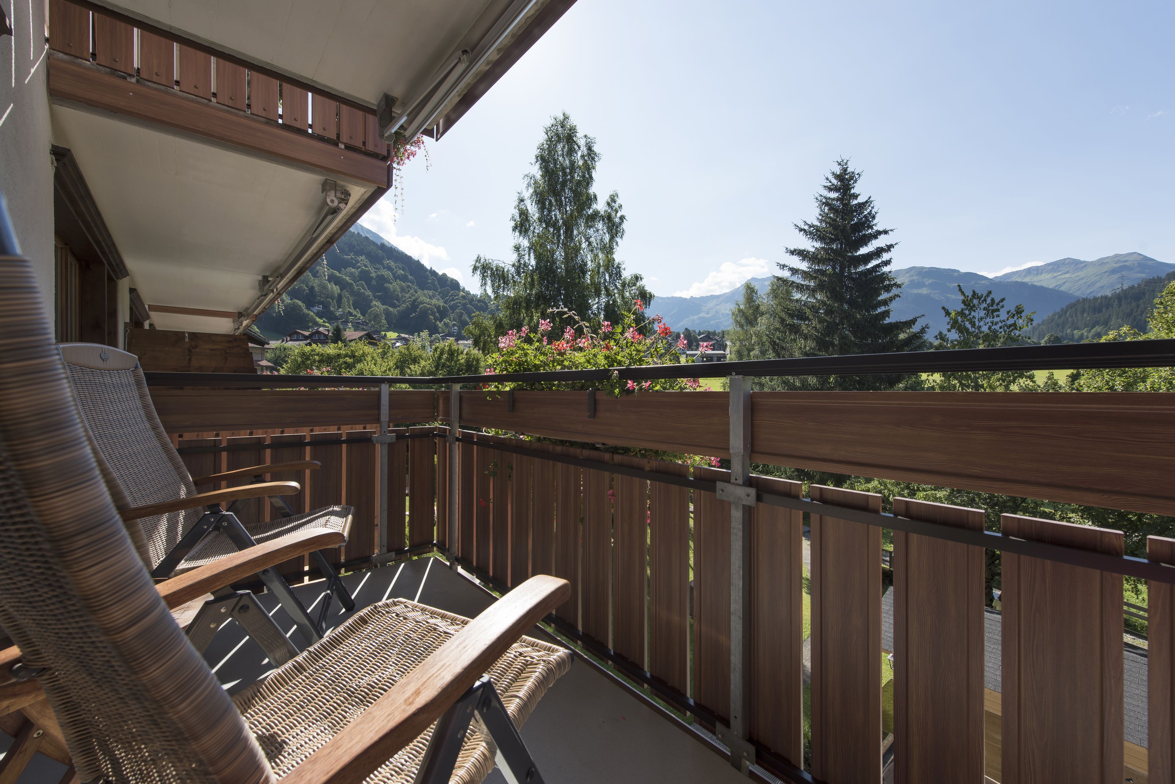 Ein Balkon mit Korbstühlen, einem Holzzaun und Blick auf Berge und Grün.