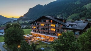 A multi-story hotel with a restaurant on the ground floor, surrounded by lush greenery and mountains in the background. - Sunstar Hotel Klosters (Klosters-Serneus)