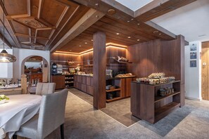 Una cocina moderna con vigas de madera, un comedor con mesa y sillas, y una exhibición de productos horneados.