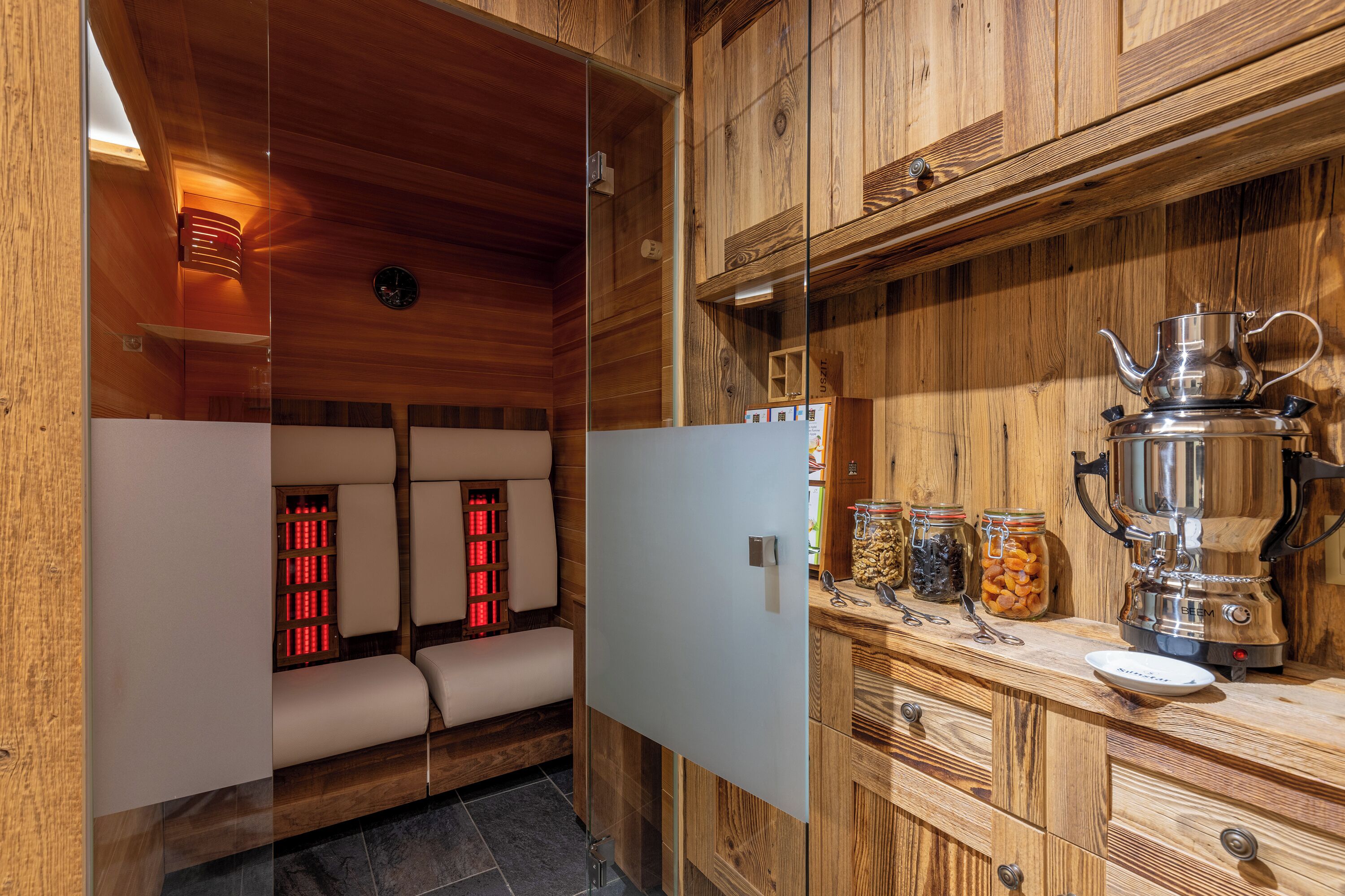 A wooden cabin interior with a sauna, a wooden cabinet with jars, and a kettle on the counter.