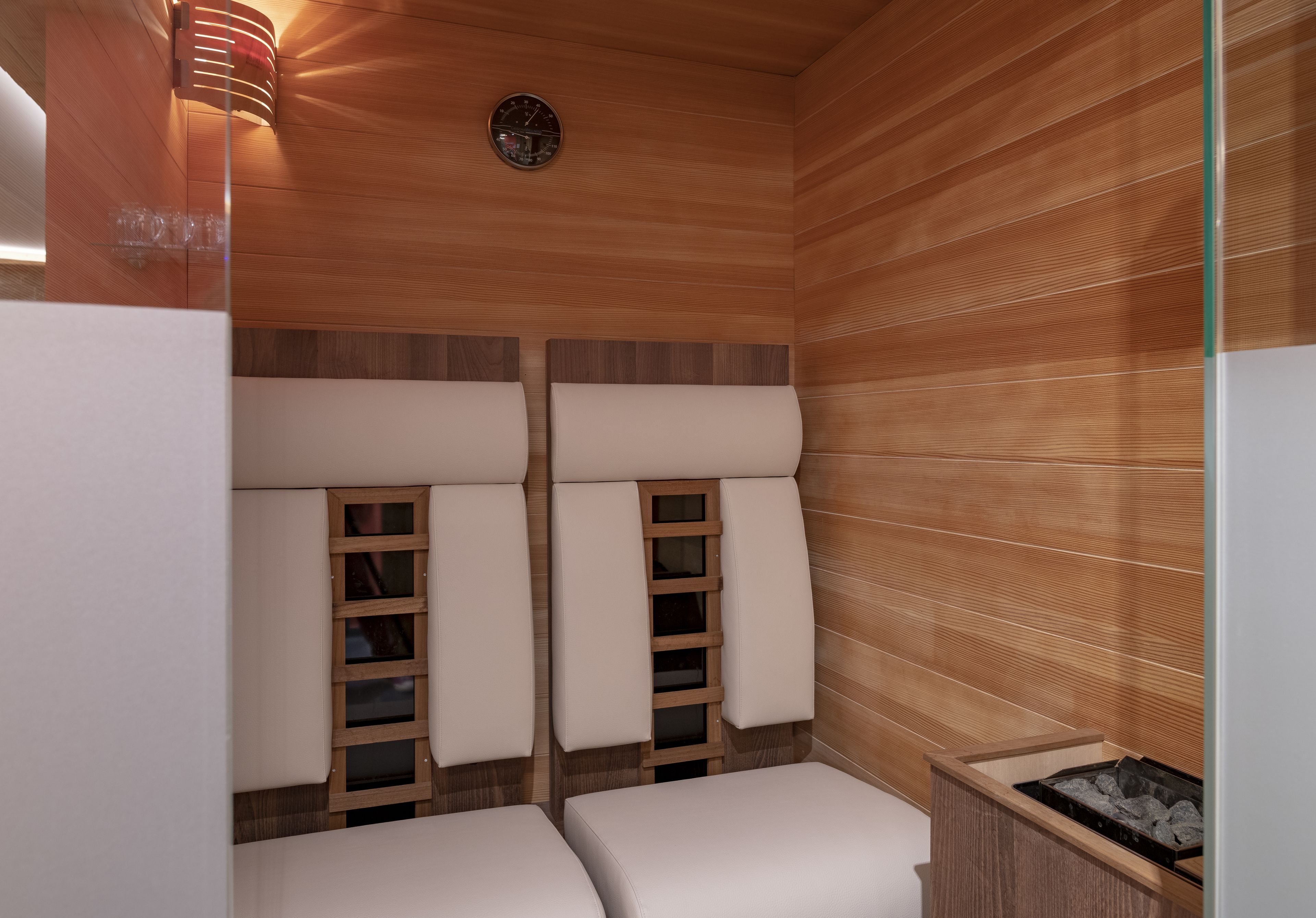 A sauna room with wooden walls, two benches, a wooden shelf, and a clock on the wall.