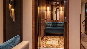 An elevator with a blue upholstered bench, wooden paneling, and a patterned carpet.