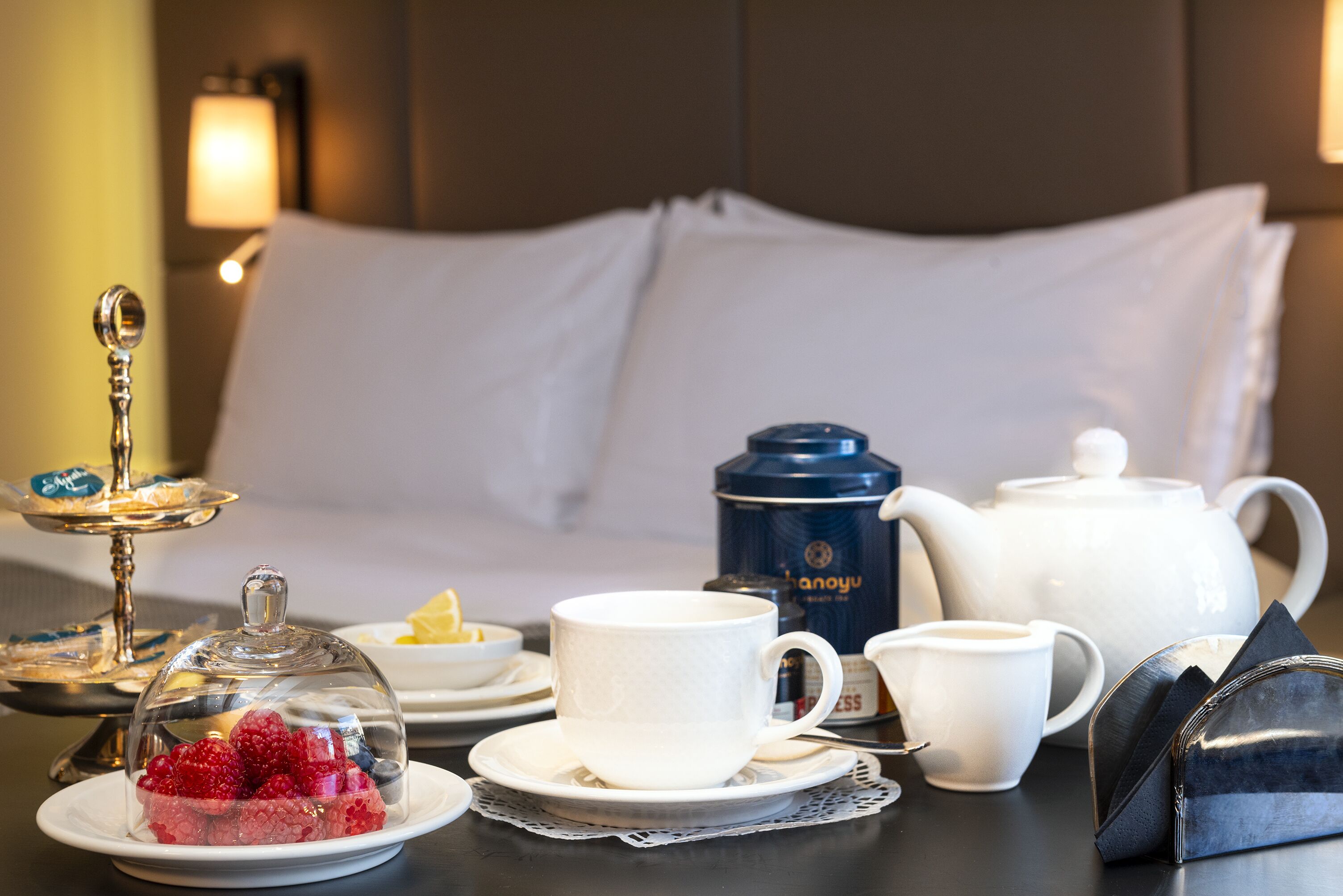 A neatly arranged breakfast table with a teapot, cups, a glass dome with berries, and a small dish with butter.
