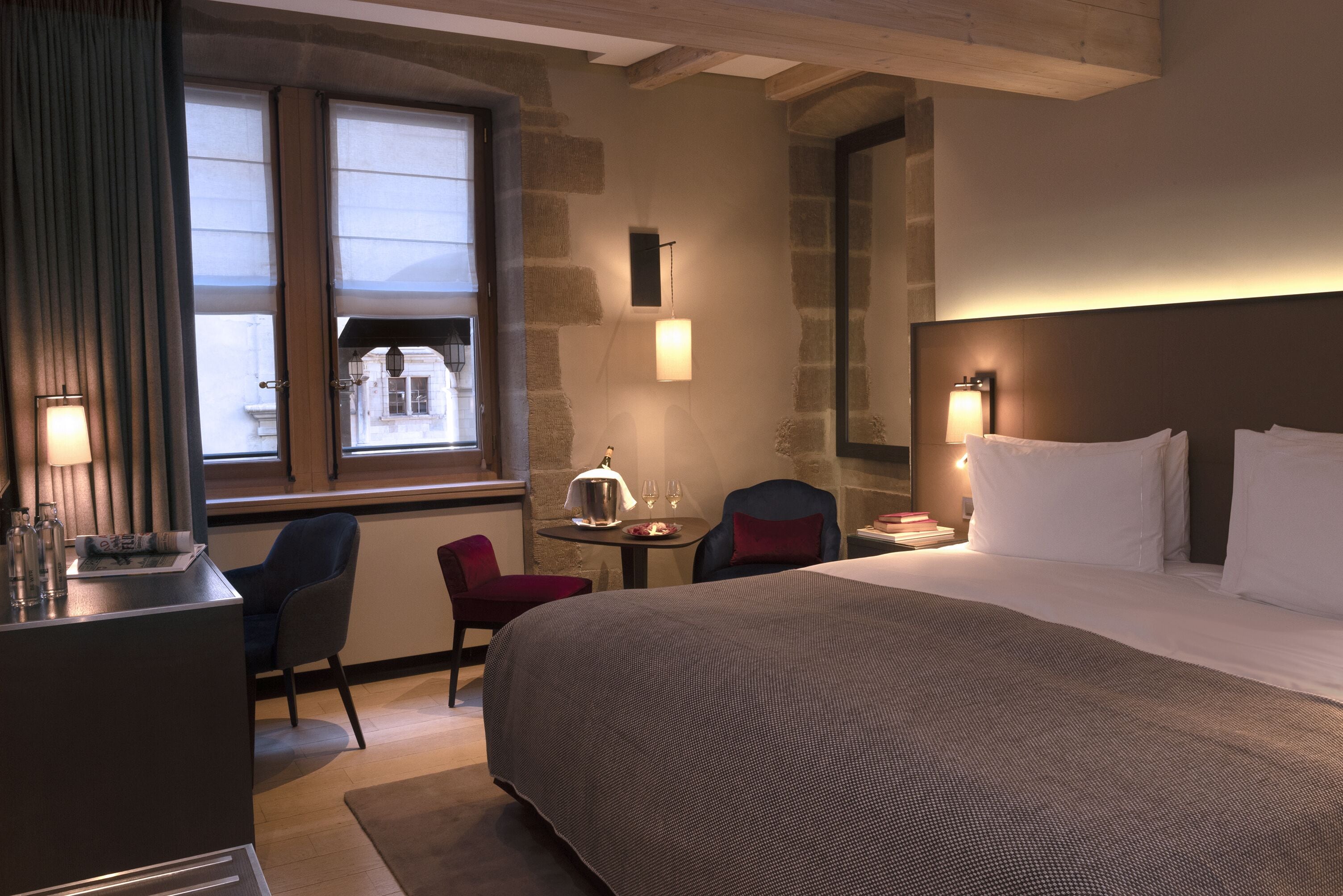 Una habitación de hotel con una cama grande, un escritorio, una silla, una mesita con lámpara y una ventana con cortinas.