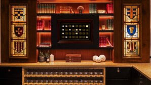 A library with bookshelves, a framed display of wine bottles, and decorative items.