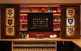 Uma biblioteca com estantes de livros, um painel decorativo com garrafas de vinho e objetos decorativos.