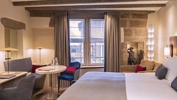 Habitación de hotel con una cama grande, un escritorio con silla, una mesita redonda y un balcón con cortinas.