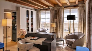 A modern hotel room with a wooden ceiling, a desk with a computer, a comfortable armchair, a bookshelf, and a large window with curtains. - Hôtel Les Armures (Geneva)